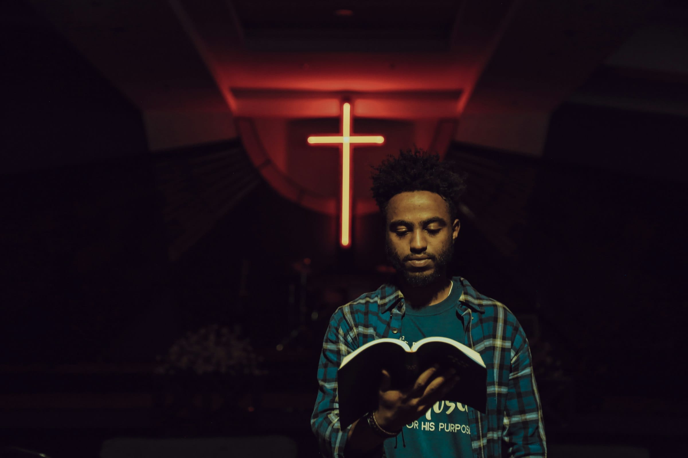 A man reading the Bible beneath a lit cross